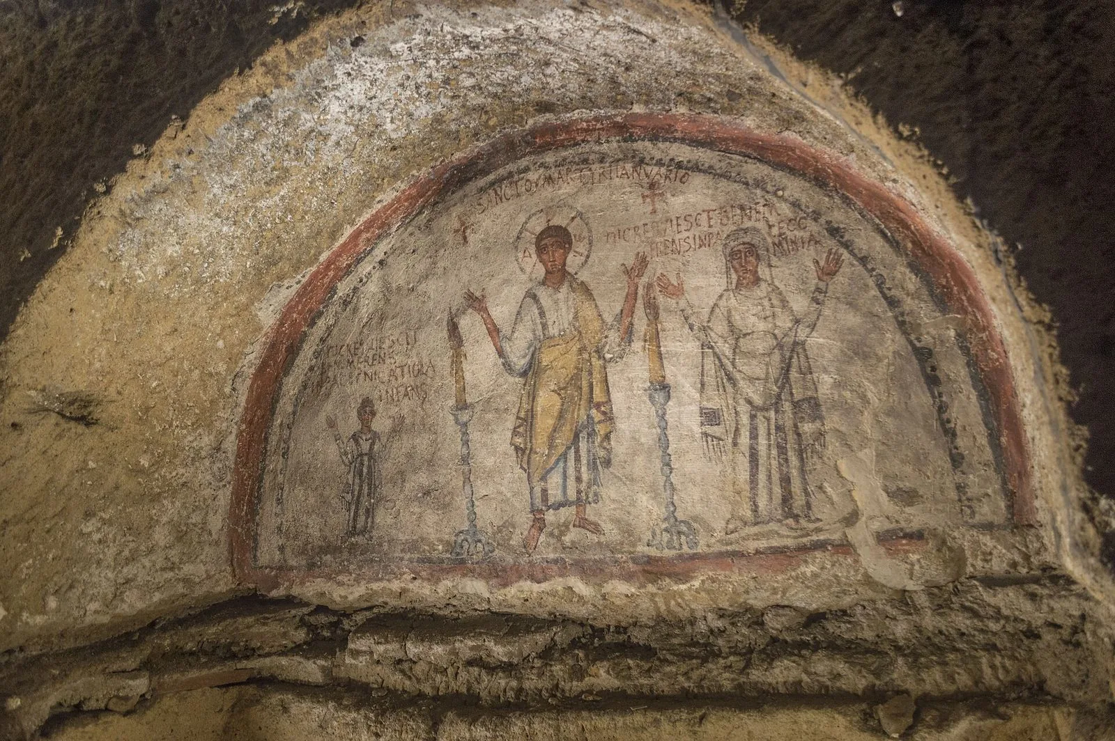Affresco paleocristiano in una lunetta delle Catacombe di San Gennaro: al centro San Gennaro con l'aureola e le braccia alzate tra due candelabri, ai lati una bambina e una donna velata, con iscrizioni in latino