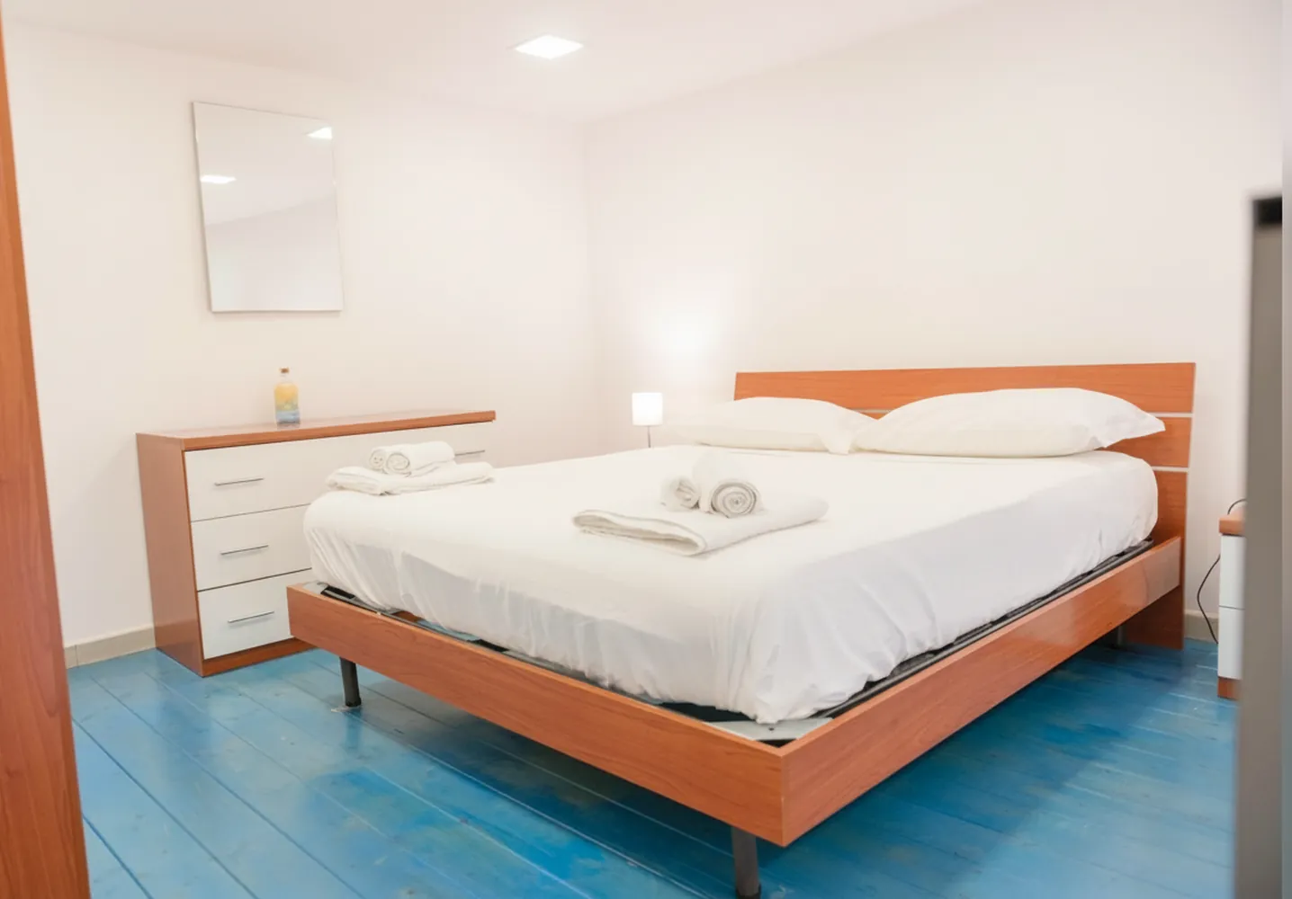 Il letto matrimoniale sul soppalco con il pavimento in legno azzurro, la cassettiera e la testiera in legno